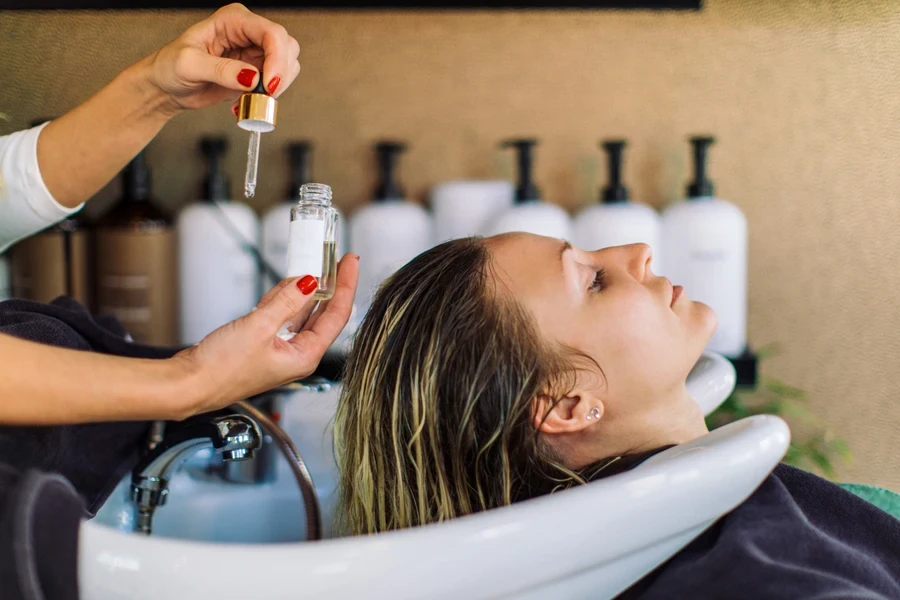 Hairdresser applying hair serum to wet hair of customer