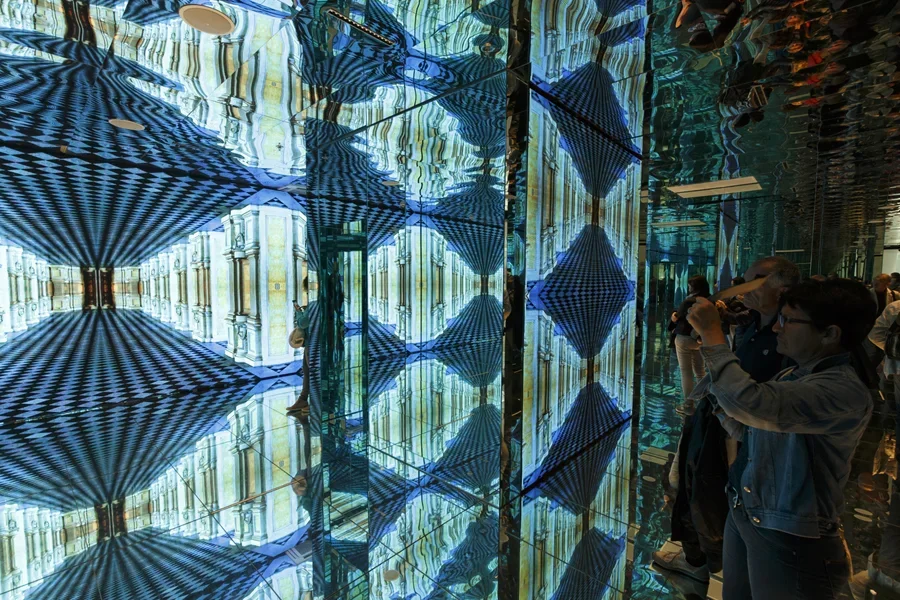 Люди любуются привлекательными экспонатами на бесконечных зеркалах на выставке