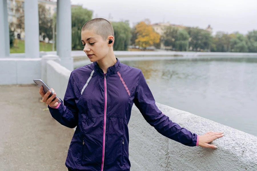 Person standing outside with earbuds in adjusting music