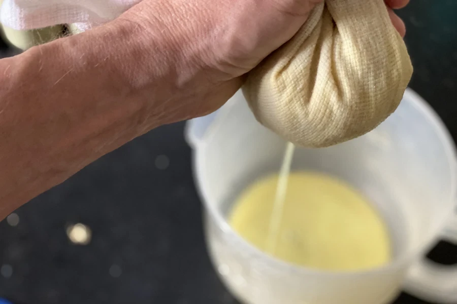 Person using cheesecloth to strain juice into plastic jug