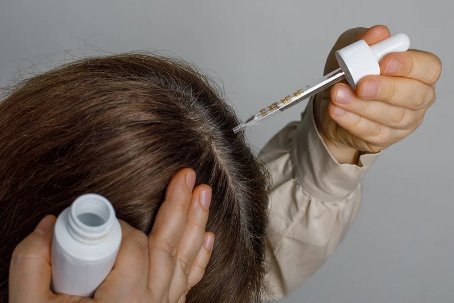 Woman applying small amount of hair serum to scalp