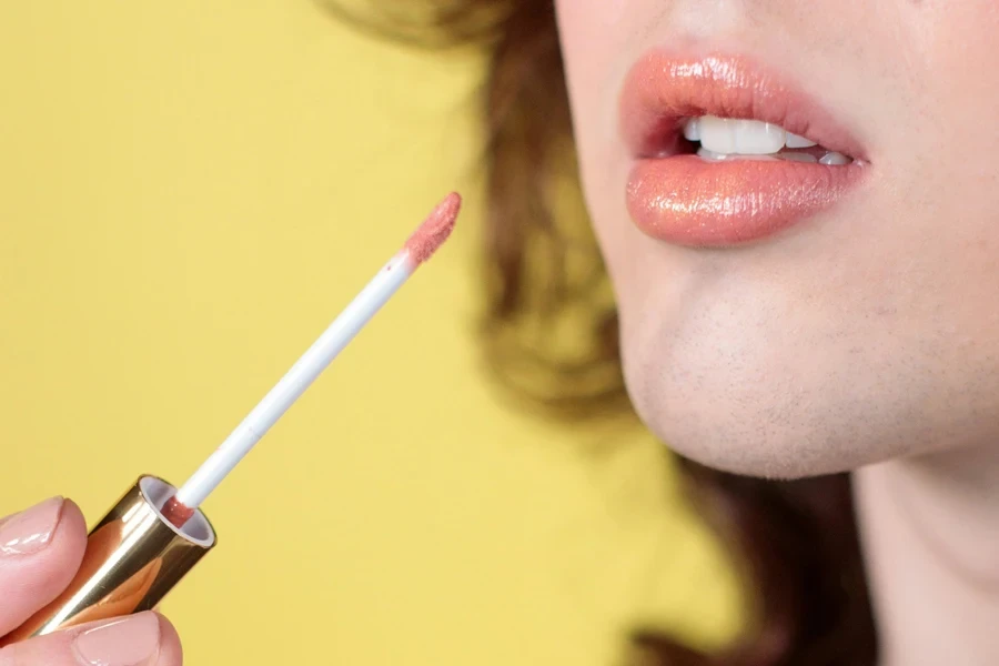 Woman holding a pink lip gloss and applying it to lips
