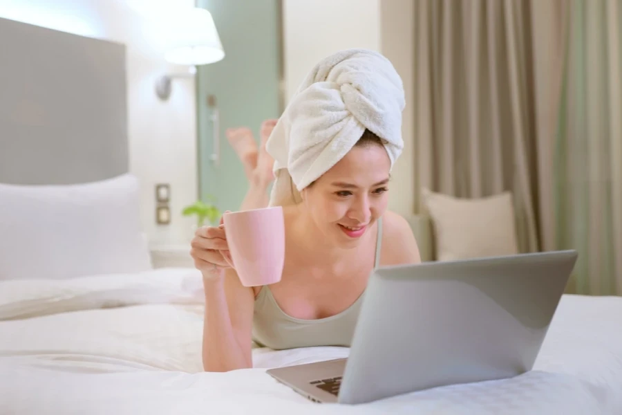 Woman with coffee and laptop open on bed