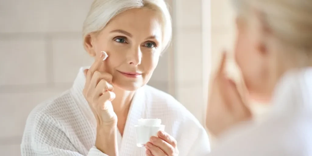 Woman with white hair applying anti aging cream to face