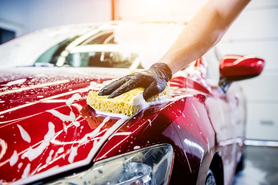 Worker washing red car with sponge on a car wash