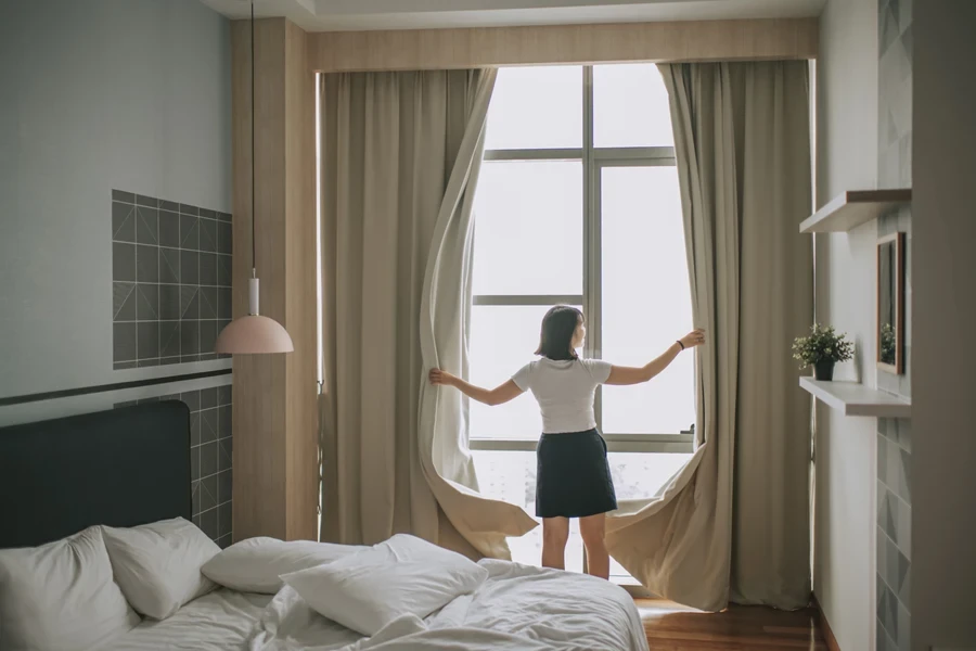 Yound lady opening bedroom curtains