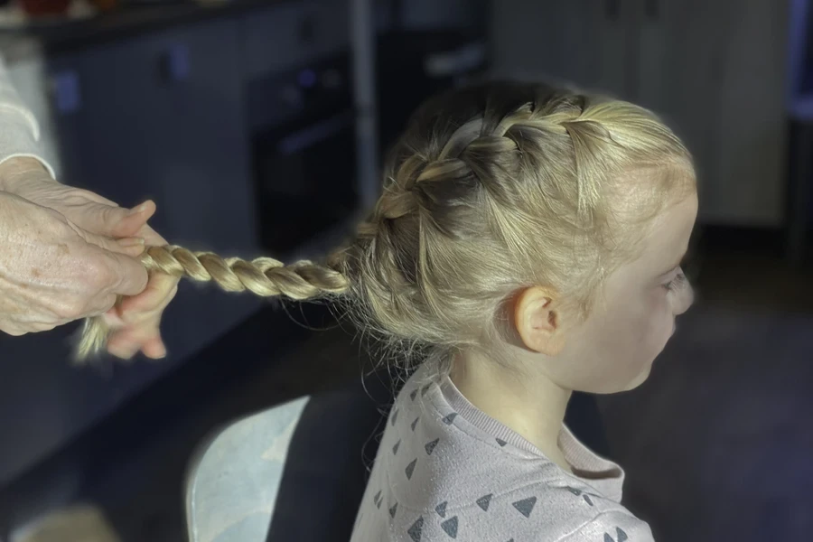 Young girl with blond hair getting Dutch braids styled