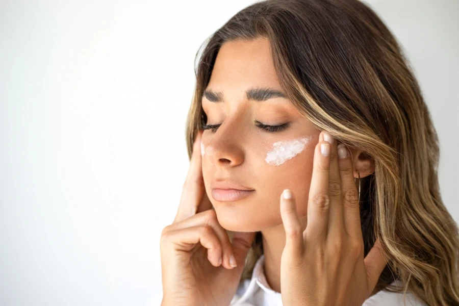Young woman applying white cream for treatment of acne