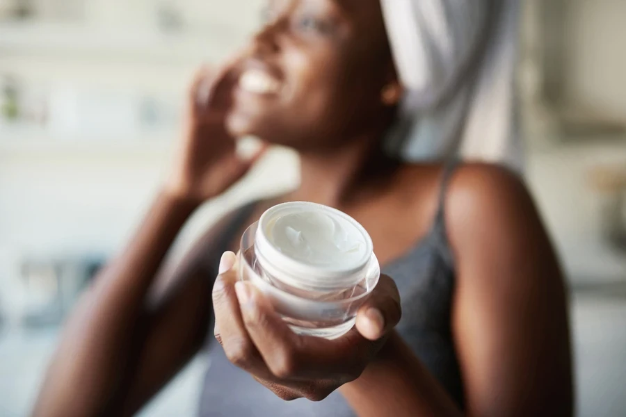 Young woman holding tub of cream while in bathrobe
