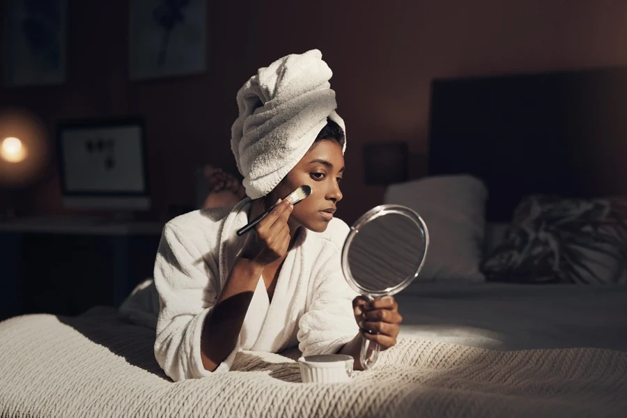 Young woman on bed looking into small mirror