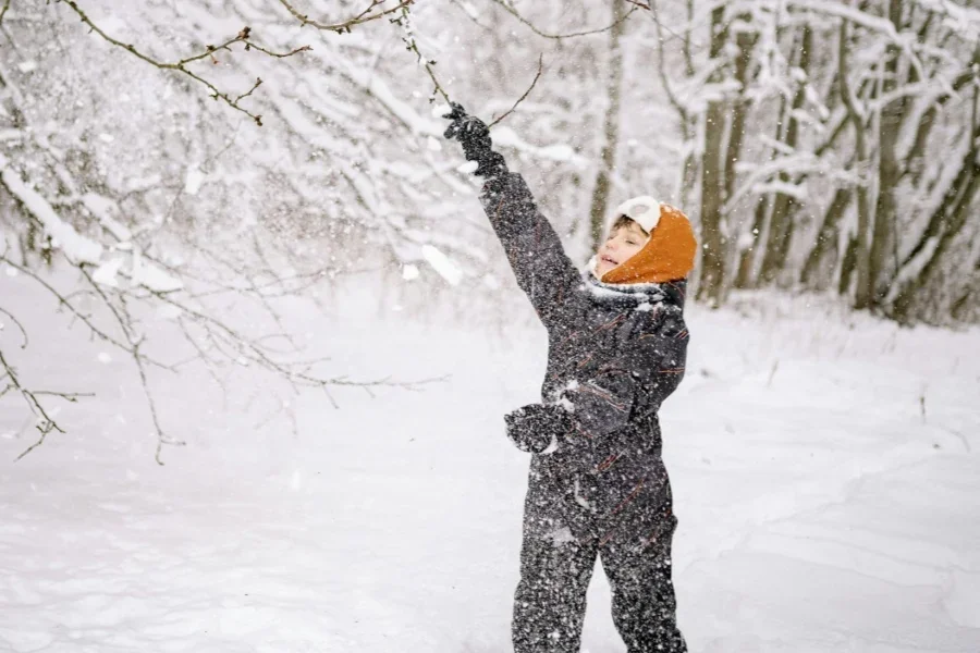 Un enfant en vêtements d'hiver jouant avec des branches d'arbres pendant l'hiver