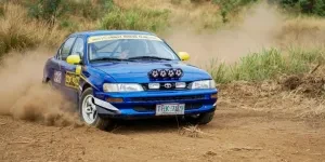 A blue car driving on a dirt road
