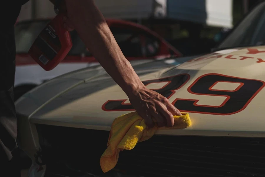 A hand with a yellow rag cleaning a car