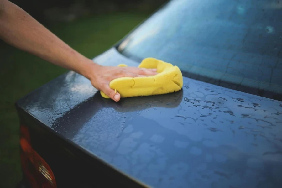 A hand with a yellow sponge cleaning a car