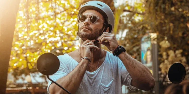 Un hombre que lleva gafas de sol y casco se ajusta la correa al aire libre bajo la luz solar brillante.