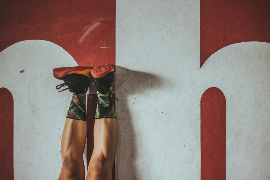 A person in colorful socks and sneakers exercising against a bold red wall