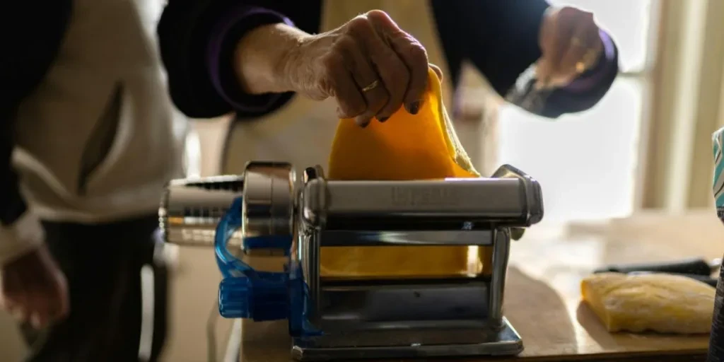 A person putting pasta sheet in a traditional pasta maker