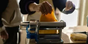 A person putting pasta sheet in a traditional pasta maker