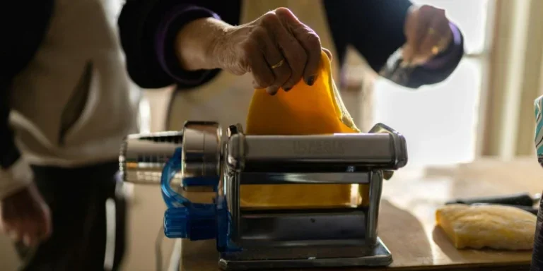 A person putting pasta sheet in a traditional pasta maker