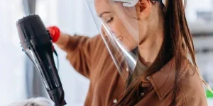 A person wearing a face shield and a blow dryer