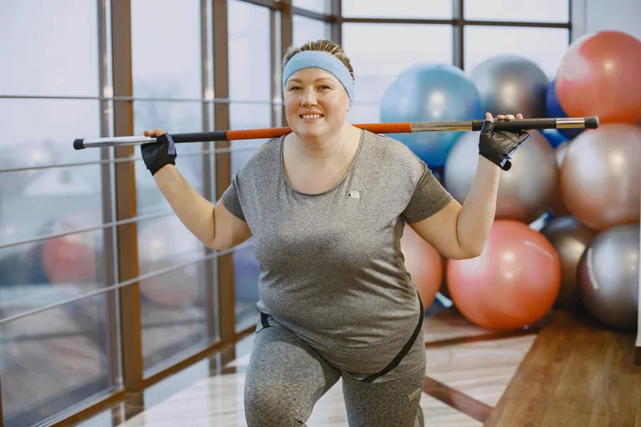 A plus-size woman in gym attire exercising with a barbell in a modern gym environment