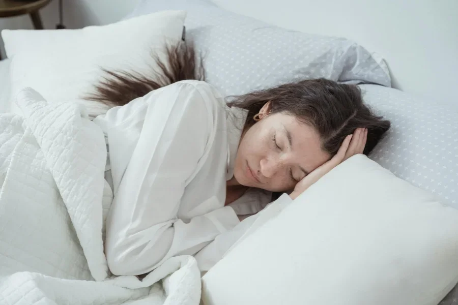 A serene woman rests comfortably in bed with soft pillows and blankets, embracing relaxation