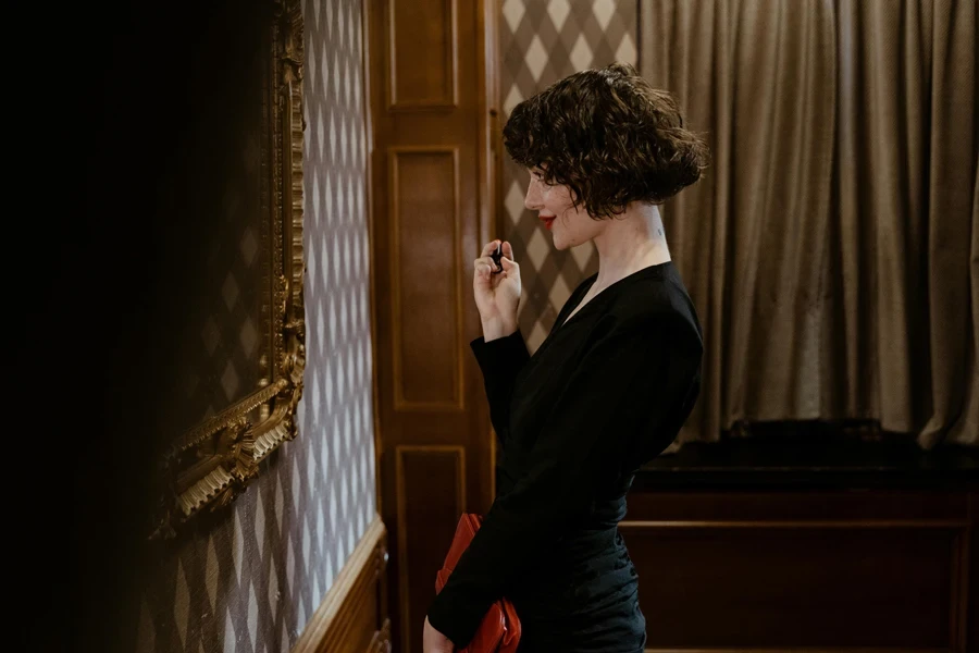 A stylish woman in a black dress admiring art in a sophisticated indoor setting