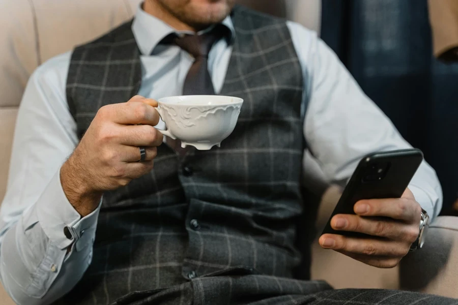 A well-dressed businessman in a checkered suit holds a smartphone and teacup, showcasing modern elegance