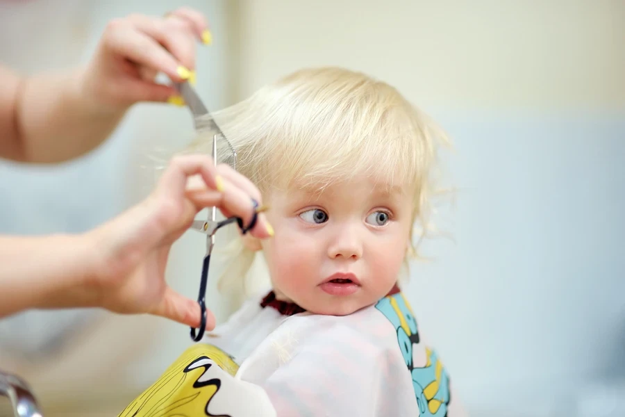 Baby with light blond hair getting hair trimmed by hairdresser