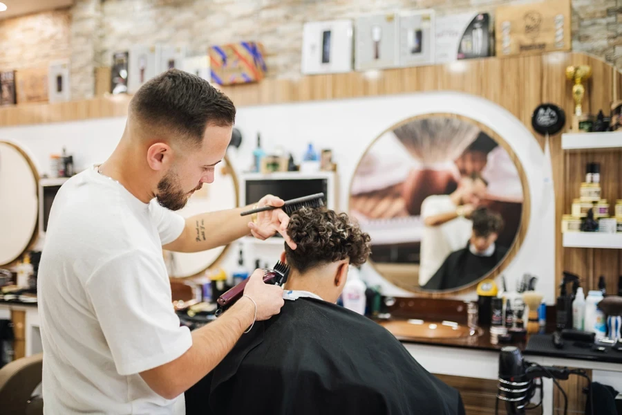 Barber using trimmer to sharpen edges of boy’s haircut