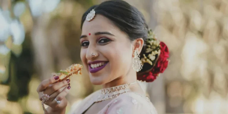 Beautiful Indian bride with traditional attire smiling while having a snack outdoors