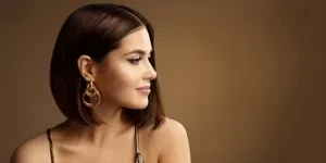 Potret Profil Wanita Cantik dengan Gaya Rambut Bob Anting Emas di atas Coklat Tua.
