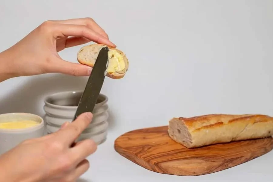 Mantequera de color beige y persona untando mantequilla sobre el pan