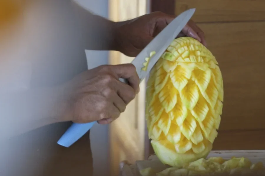 Der Koch schneidet mit einem Tranchiermesser schöne Muster aus einer Ananas