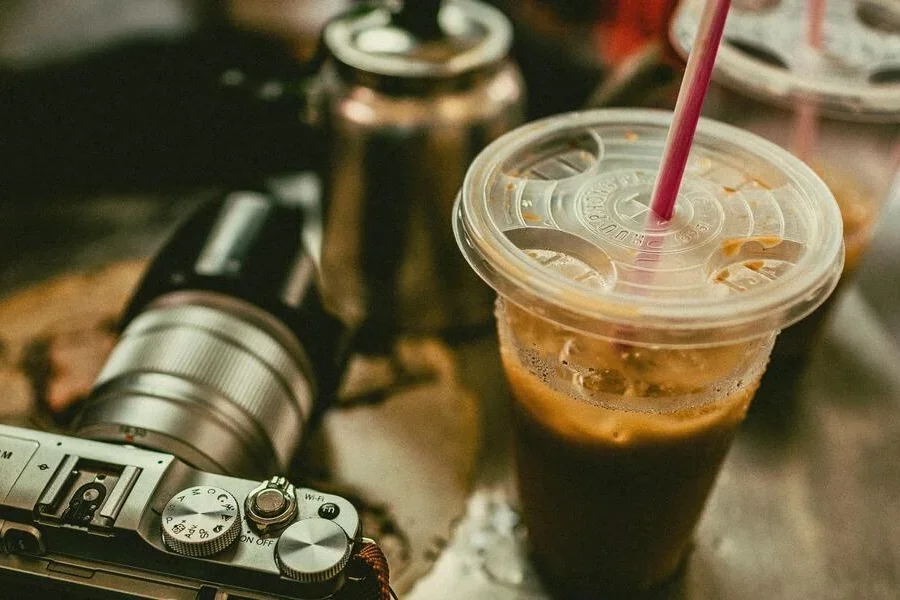 Coffee in single-use plastic containers next to a camera
