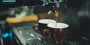 Pembuat kopi menuangkan kopi ke dalam cangkir coklat
