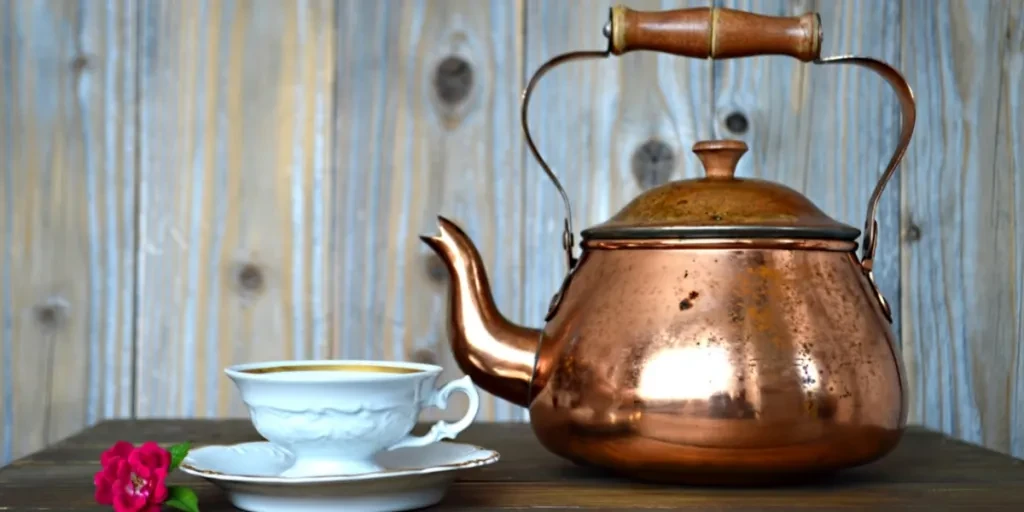 Copper kettle with wood handle next to teacup on table