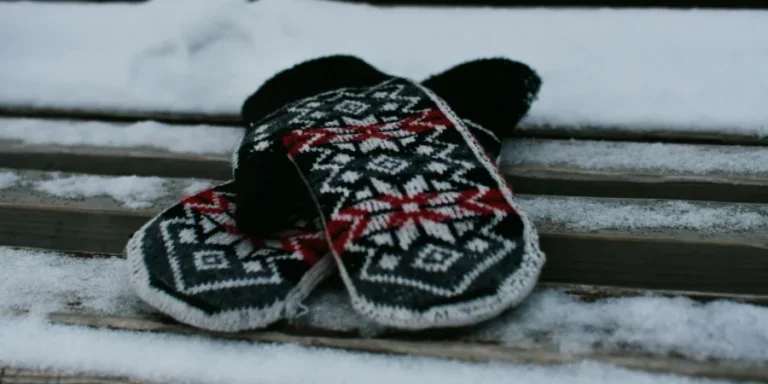 Acogedores mitones de punto con estampado nórdico descansan sobre un banco nevado en invierno