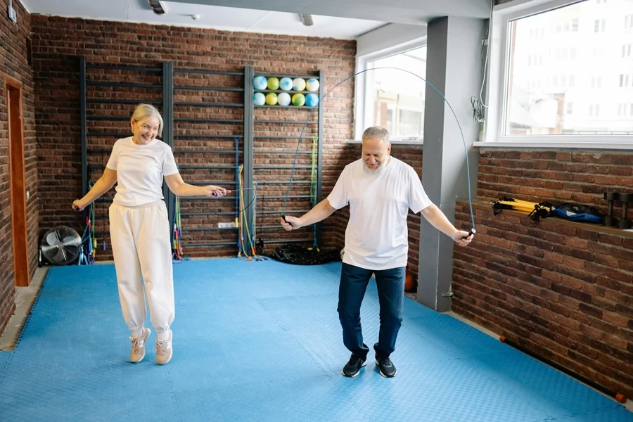 Elderly man and woman joyfully jump rope in a bright gym promoting a healthy lifestyle
