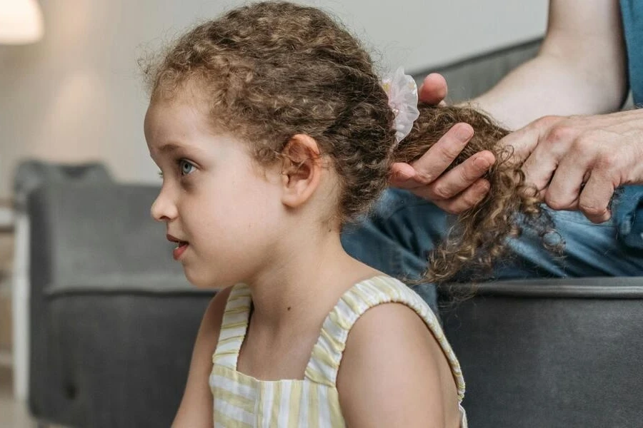 Hands of a person styling a girl’s curly hair
