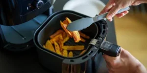 Hands put fries into a black air fryer on a kitchen counter.