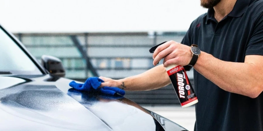 Man using cloth and spray to clean and detail a car hood outdoors