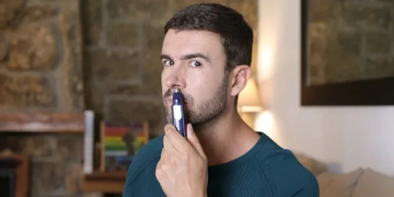 Мужчина пользуется триммером для стрижки волос в носу дома.