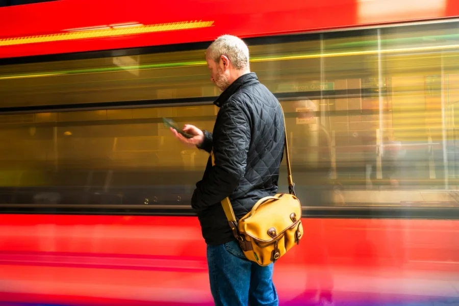 Pendler mittleren Alters mit Blick auf Smartphone mit rasenden Zug Bewegungsunschärfe