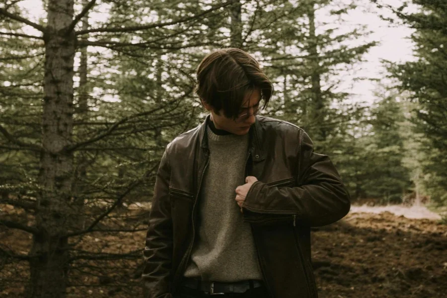 Model in a Leather Jacket and Gray Sweater Standing in the Forest