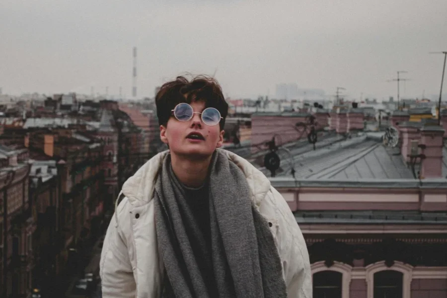 Fotografía de una mujer con gafas redondas y tejados de la ciudad al fondo
