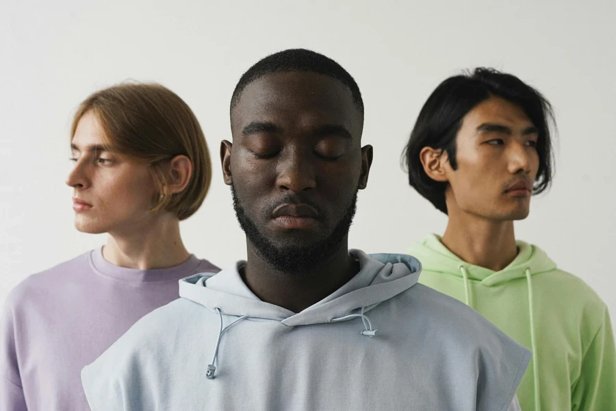 Portrait of three diverse young men wearing casual hoodies, eyes closed, against a white background