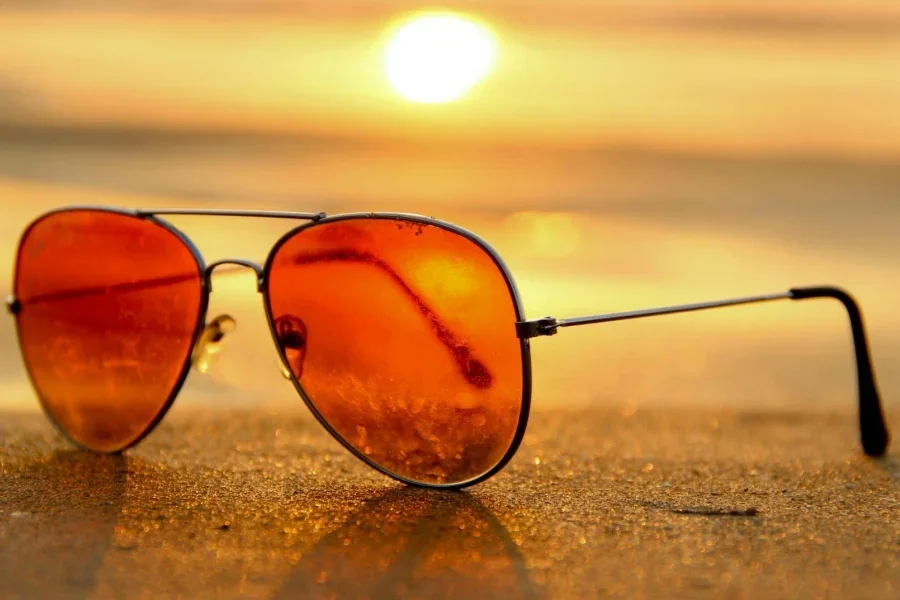 Gafas de sol rojas sobre la arena cerca del mar al atardecer. Fotografía con enfoque selectivo.