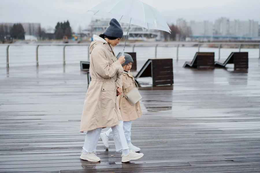 Side view of a woman and child walking together under an umbrella on a wet boardwalk
