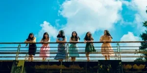 Six women stand on a bridge under a bright blue sky, enjoying a sunny day outdoors